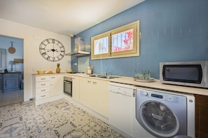 A kitchen with a clock, microwave, dishwasher, and washing machine. - Villa Descanso - Plusholidays (Calpe / Calp)