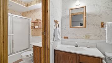 A bathroom with a toilet, sink, mirror, and wooden cabinets.
