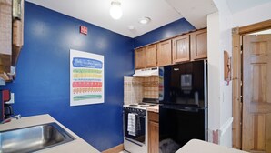 A kitchen with blue walls, wooden cabinets, a white countertop, a stove, and a black refrigerator. - The Arlington GB: Charming Centrally Located Condo in Chautauqua Institution! (Chautauqua)