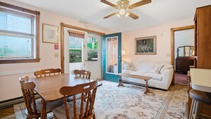A room with a dining table, chairs, a sofa, a ceiling fan, and a patterned rug. - The Arlington GB: Charming Centrally Located Condo in Chautauqua Institution! (Chautauqua)