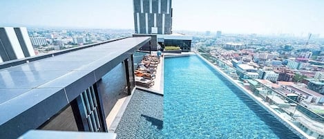 Piscina en la azotea con sillones de descanso y vistas a la ciudad.