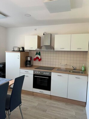 Eine moderne Küche mit weißen Schränken, einem Herd, einem Backofen und einer Kaffeemaschine.