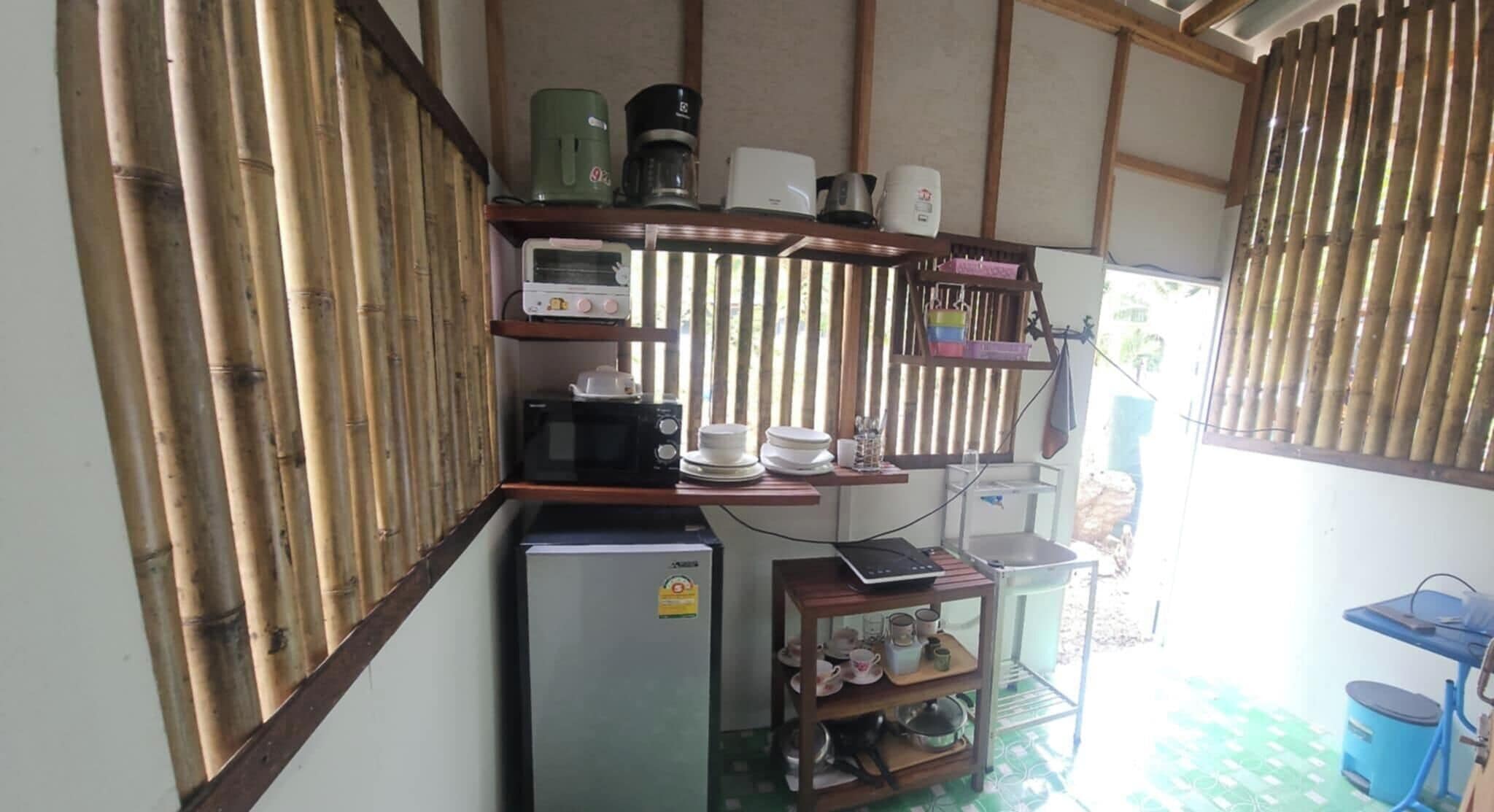 A compact kitchen with a refrigerator, microwave, coffee maker, and shelves with dishes and utensils.