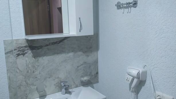 A bathroom with a white sink, a mirror, a towel rack, and a hairdryer. - ALPEDE (Zestafoni)