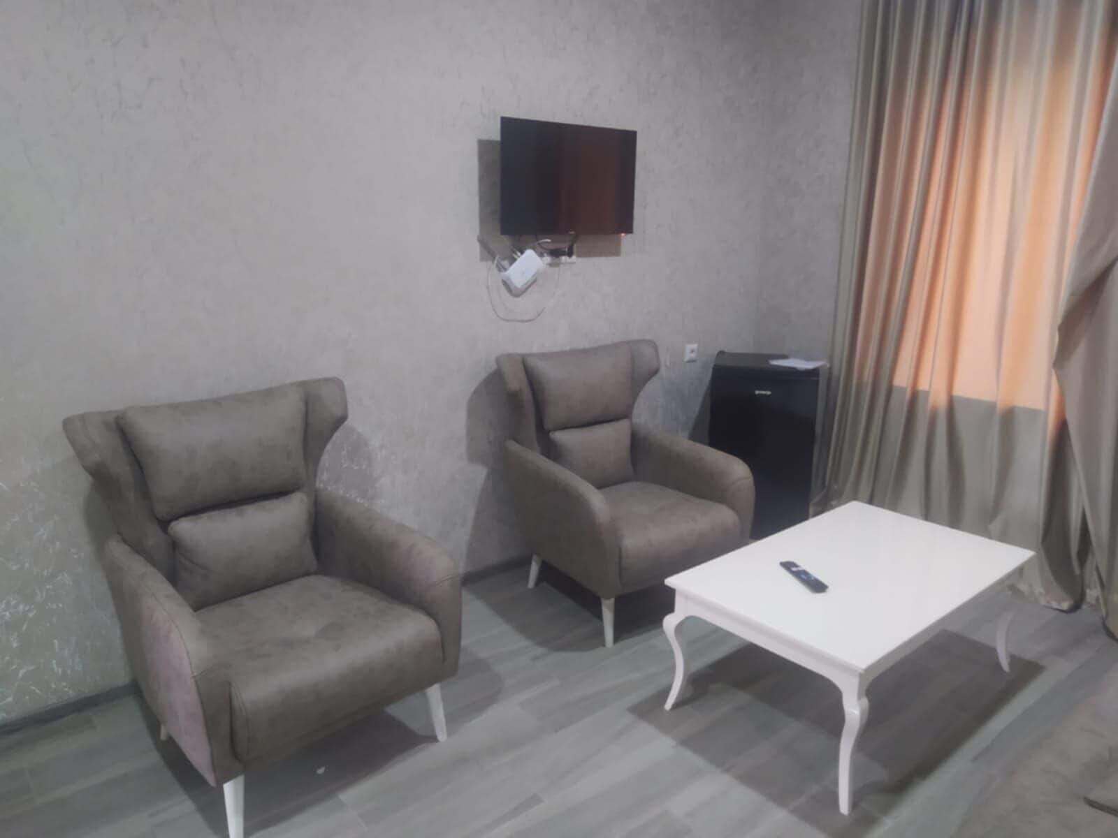 A room with two armchairs, a small table, a television mounted on the wall, and a dark-colored cabinet.