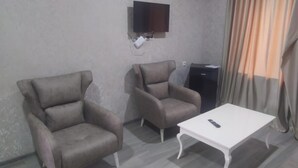 A room with two armchairs, a small table, a television mounted on the wall, and a dark-colored cabinet. - ALPEDE (Zestafoni)