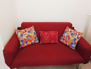 A red sofa with three pillows, one with a floral pattern and two with a patchwork design. - Bright Two-Room Apartment in Syracuse Near Ortigia & the Sea (Siracusa)