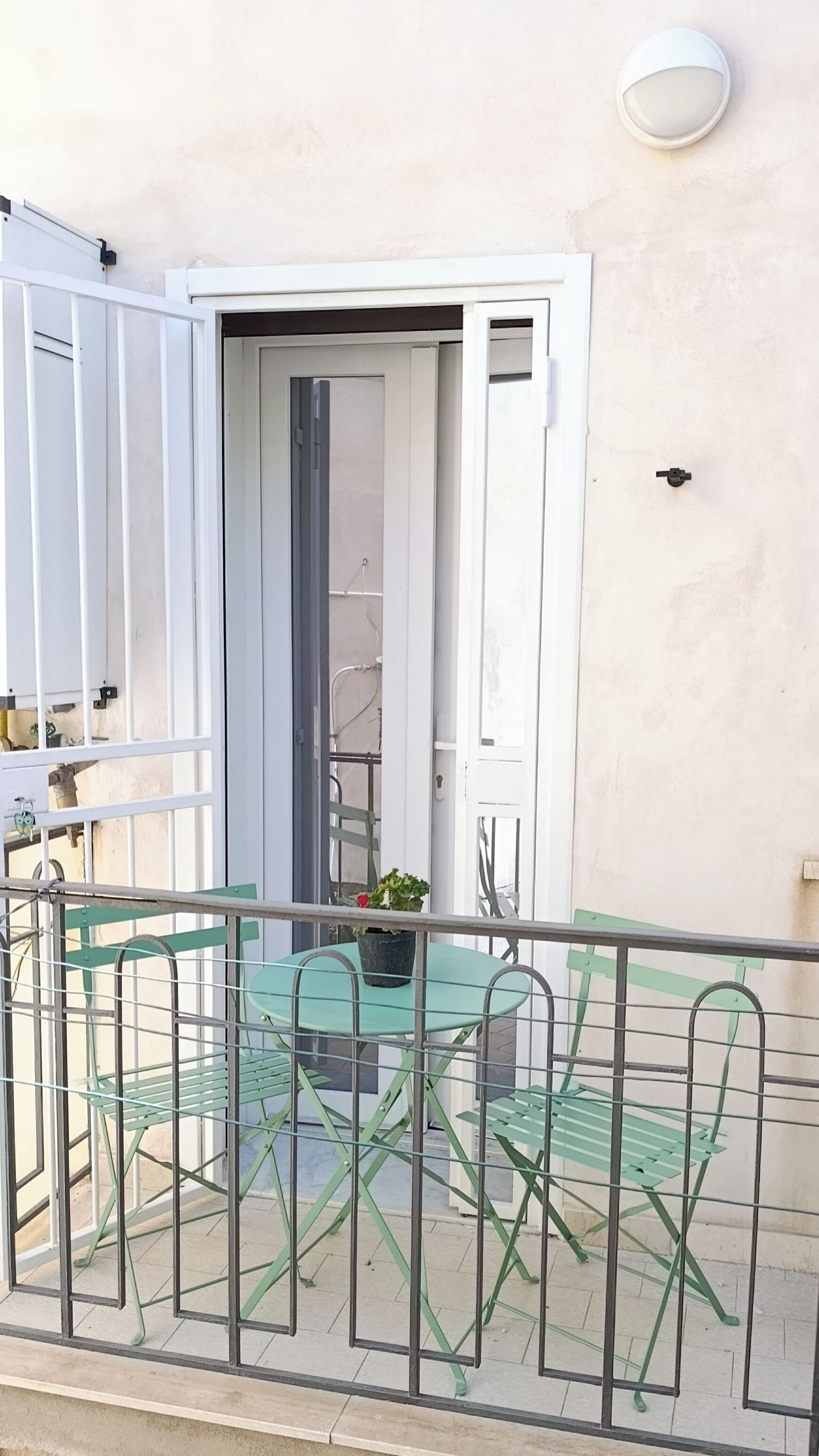 An outdoor balcony with a table and chairs, a potted plant, and a door leading to an interior space.