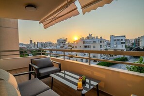 Een balkon met een tafel, stoelen en een uitzicht op de stad bij zonsondergang.