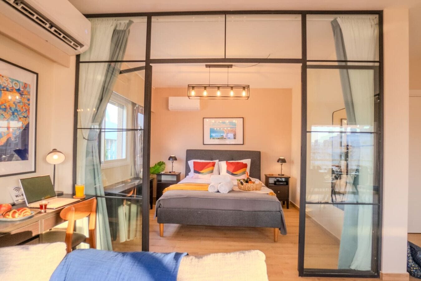 Een moderne hotelkamer met een groot bed, een bureau met een laptop en uitzicht door een glazen scheiding.
