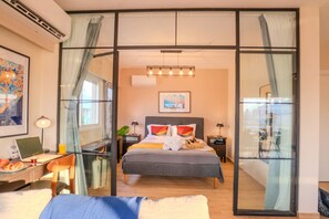 Une chambre d’hôtel moderne avec un grand lit, un bureau avec un ordinateur portable et une vue dégagée grâce à une paroi en verre.