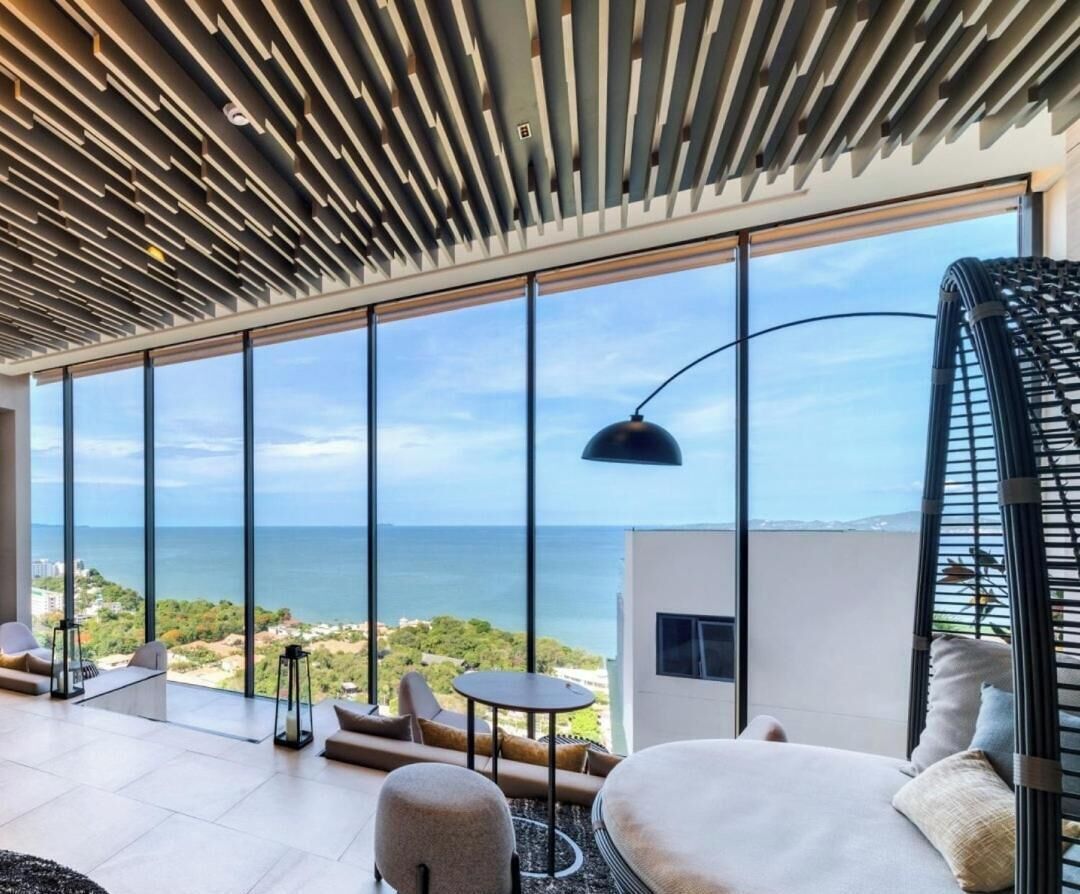A modern interior with large windows, a ceiling with linear patterns, and a view of the sea.
