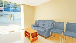 Un área de espera con un sofá y sillones, una pequeña mesa de madera, y un ventanal con vistas al exterior.