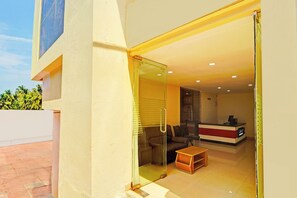 A modern interior with a reception desk, seating area, and a glass door leading to an outdoor space. - Collection O Surathkal Beach (Surathkal)