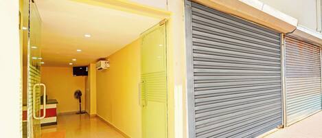 A hallway with a closed metal shutter door, a glass door entrance, and a fan in the corner.