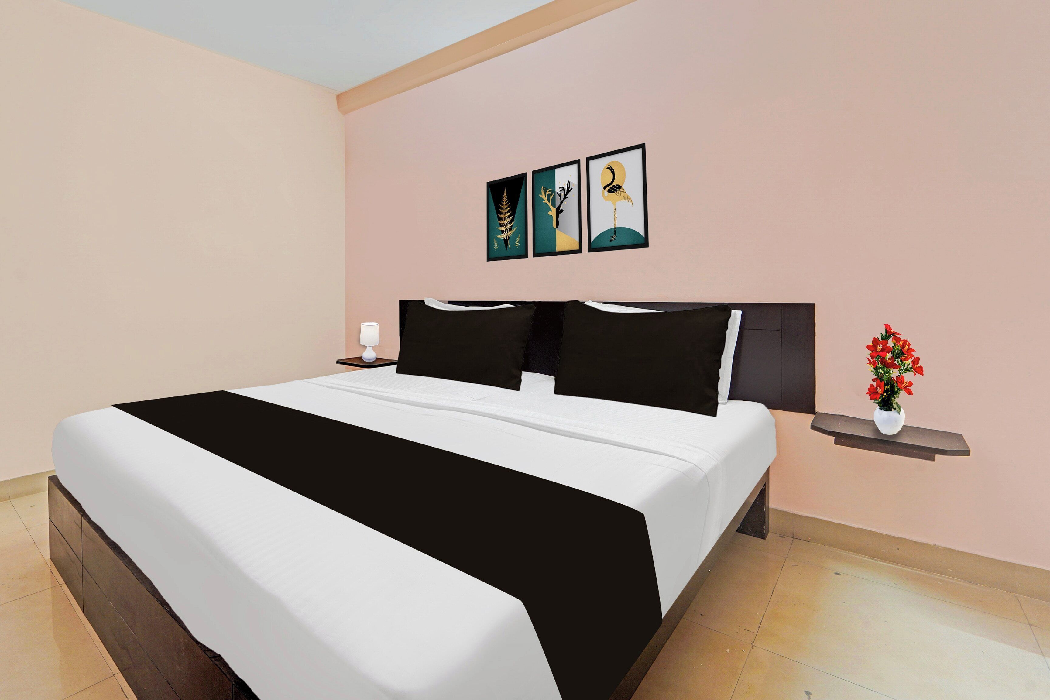 A bedroom with a bed, a nightstand, a lamp, and a wall-mounted shelf with a vase of flowers.