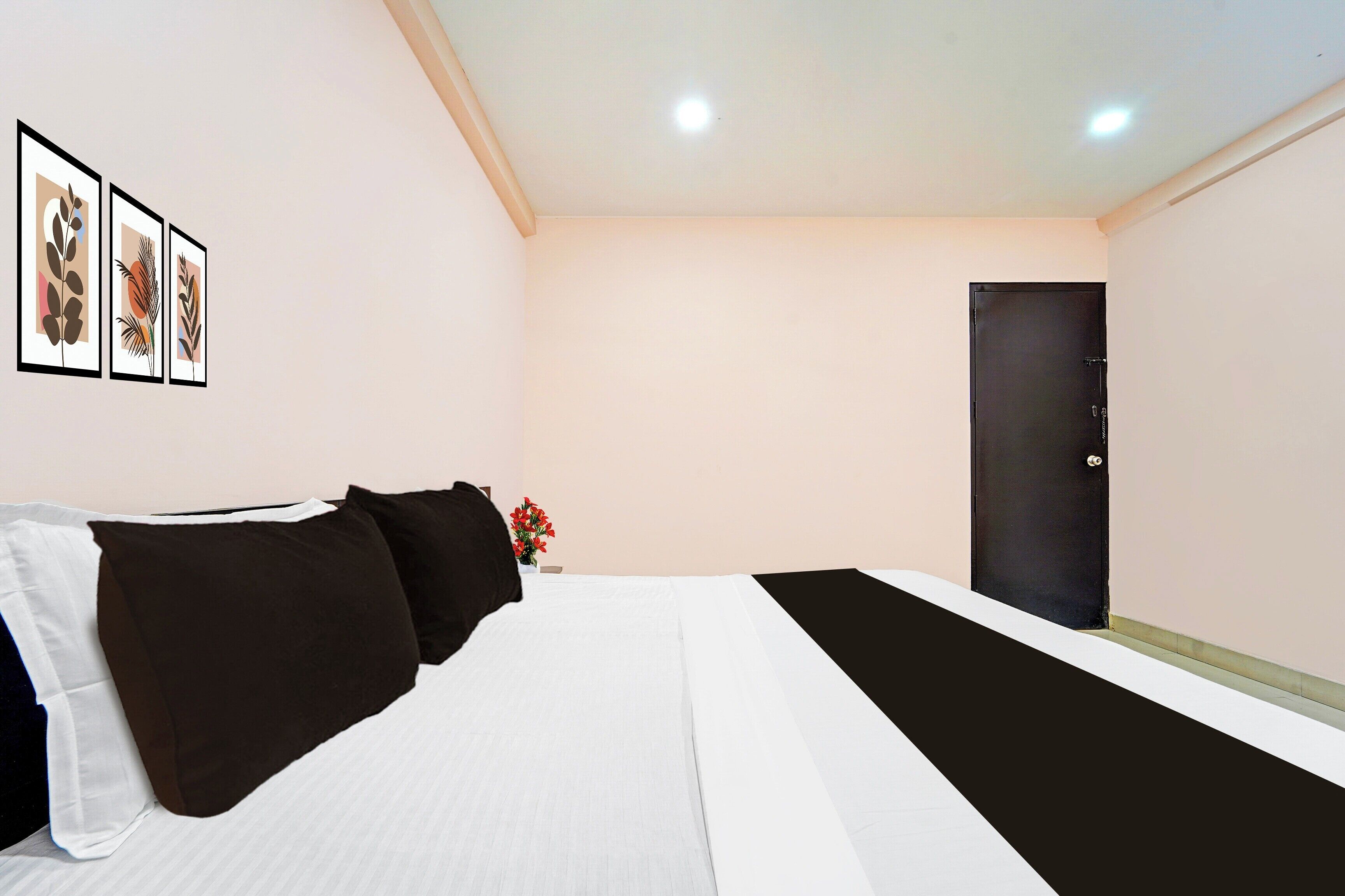 A hotel room with a bed, a black door, and three framed pictures on the wall.
