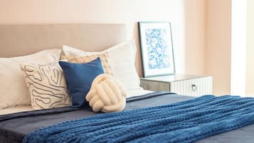 Un lit bien fait, recouvert d’une couverture bleu foncé, avec un coussin décoratif et un cadre photo accroché au mur.