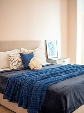 Una cama bien tendida con un edredón azul oscuro, un cojín decorativo y un cuadro colgado en la pared.
