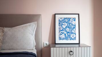 A bedroom with a bed, pillows, a bedside table with a framed picture, and a wall socket.