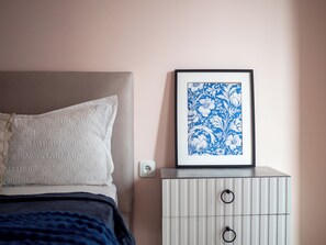 A bedroom with a bed, pillows, a bedside table with a framed picture, and a wall socket. - Cozy apartments neat Mega Alma-Ata (Almaty)