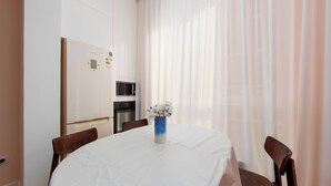Uma sala de jantar com uma mesa redonda, cadeiras, um vaso com flores, uma geladeira, um forno e um micro-ondas.