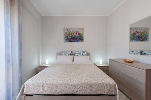 Une chambre à coucher comprenant un lit, des tables de chevet, une commode et deux tableaux accrochés au mur.