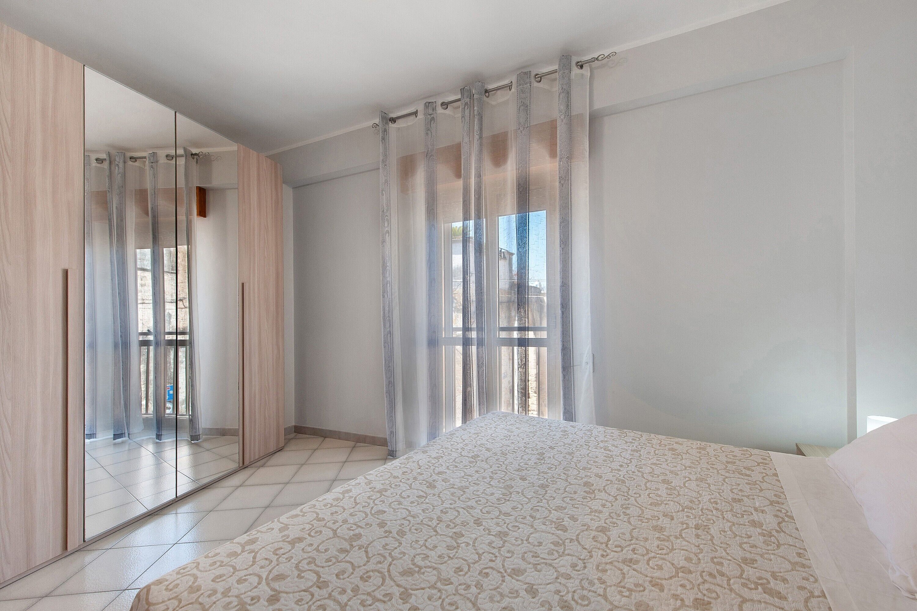 Ein Schlafzimmer mit Bett, Kleiderschrank und einem großen Fenster mit Vorhängen.