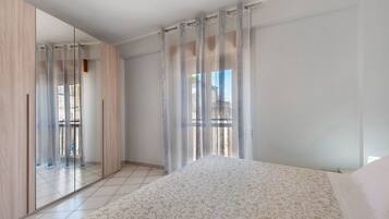 Ein Schlafzimmer mit Bett, Kleiderschrank und einem großen Fenster mit Vorhängen.