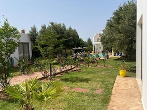 A pool area with lounge chairs and umbrellas, surrounded by greenery and a pathway.