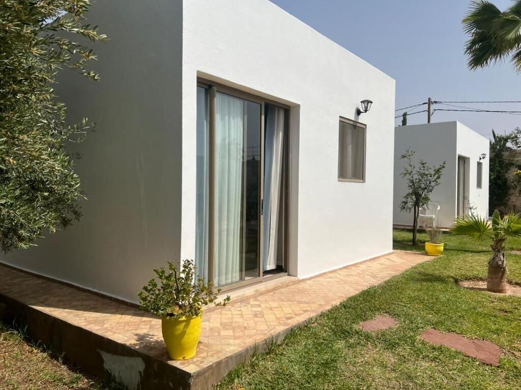 Un edificio moderno con fachada plana, grandes puertas correderas de vidrio y una ventana pequeña. En el suelo, hay una jardinera amarilla con una planta.
