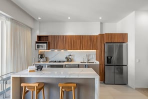 A modern kitchen with a marble island, wooden cabinets, stainless steel appliances, and a built-in oven. - 3BR condo near the ocean in Bucerías with pool, WiFi & full kitchen (Bucerias)