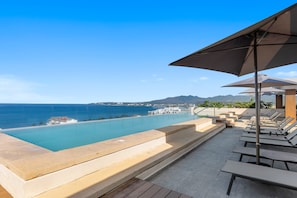 An infinity pool with a view of the ocean and distant mountains, surrounded by lounge chairs and umbrellas. - 3BR condo near the ocean in Bucerías with pool, WiFi & full kitchen (Bucerias)
