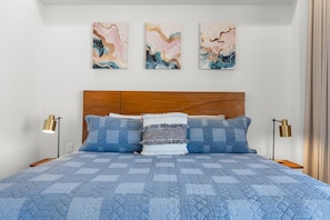 A bedroom with a wooden headboard, a blue quilted bedspread, and three abstract paintings on the wall. - Luxury 2BR Lock-Off | Rooftop Pool | Golden Zone (Nuevo Vallarta)
