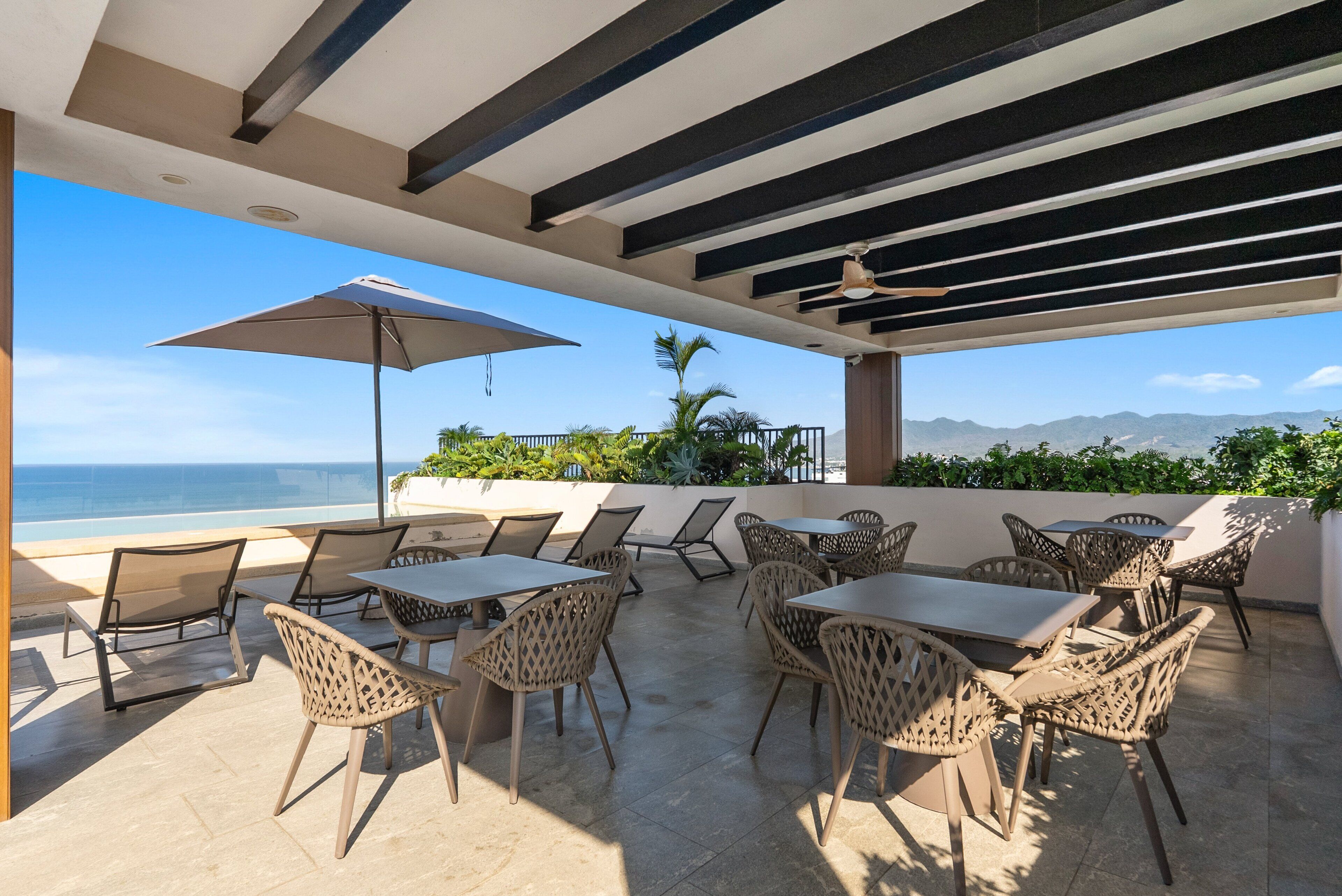 An outdoor patio with tables and chairs, a ceiling fan, and a view of the ocean.