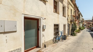 A narrow street with a building featuring a large glass door, a bicycle parked outside, and a clear sky. - Estay - The Corner House Cagliari Room 1 (Cagliari)