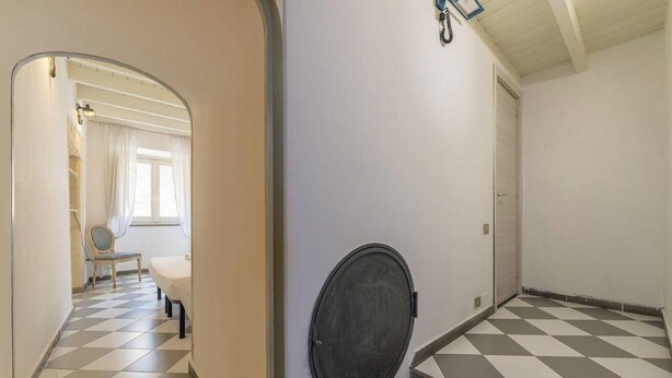 A hallway with a checkered floor, a mirror, and a door leading to a room with a window and curtains. - Estay - The Corner House Cagliari Room 1 (Cagliari)