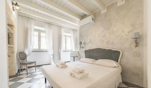Een hotelkamer met een bed, een stoel, een raam met gordijnen, een wandlamp en een geruite vloer.