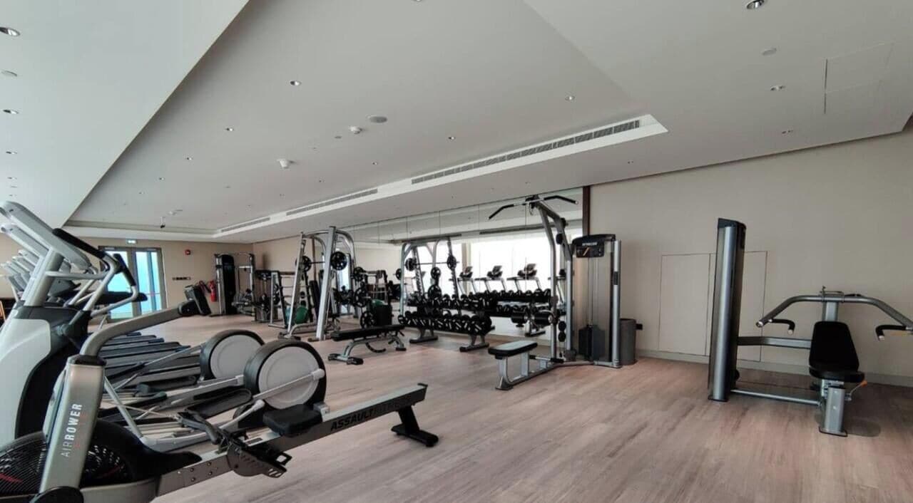 Une salle de sport moderne équipée de machines de cardio, de poids libres et d’un mur entièrement recouvert de miroirs.