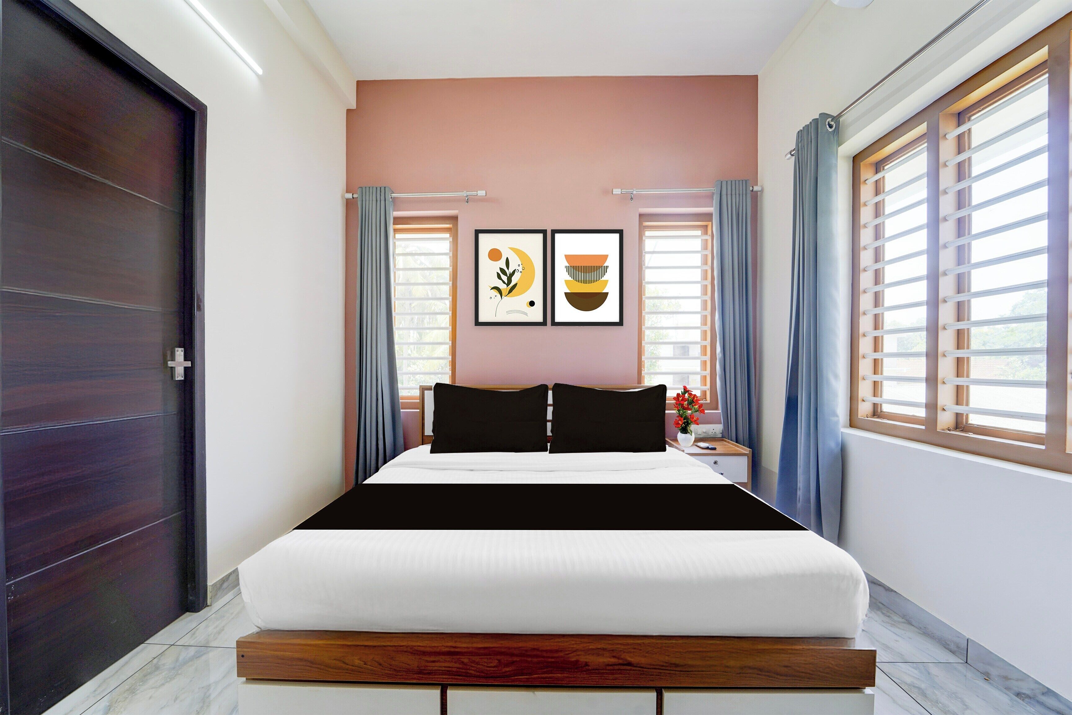 Una habitación de hotel con una cama, una mesita de noche, una ventana con cortinas y dos cuadros en la pared.