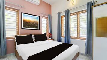 Una habitación de hotel con una cama, un cuadro en la pared y dos ventanas con cortinas.