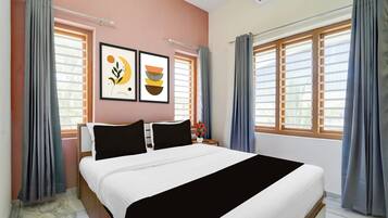 Habitación de hotel con cama, dos cuadros enmarcados, una mesita de noche y una ventana con cortinas.