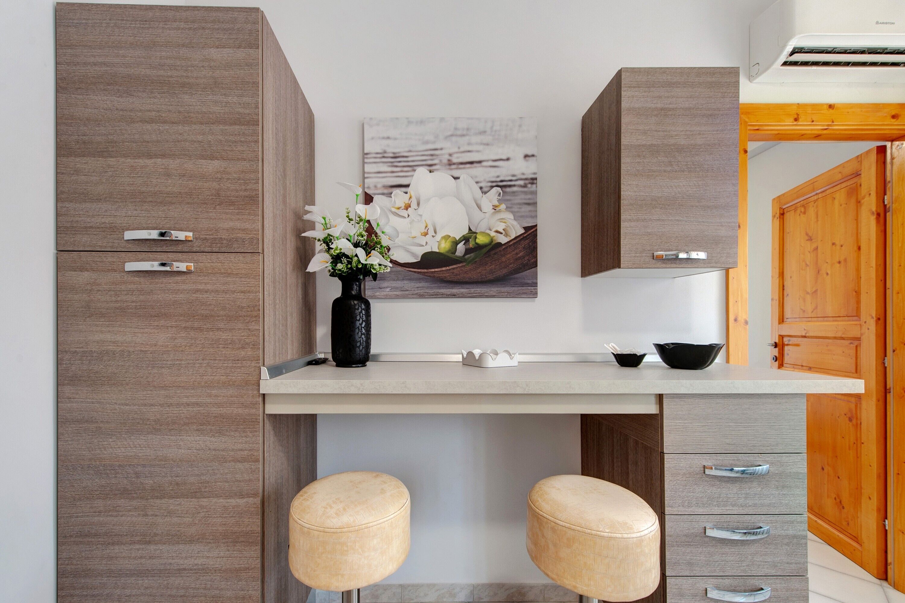 Eine moderne Küche mit einem Holzkorpus, einer weißen Arbeitsplatte, einer Vase mit Blumen und zwei Barhocker.