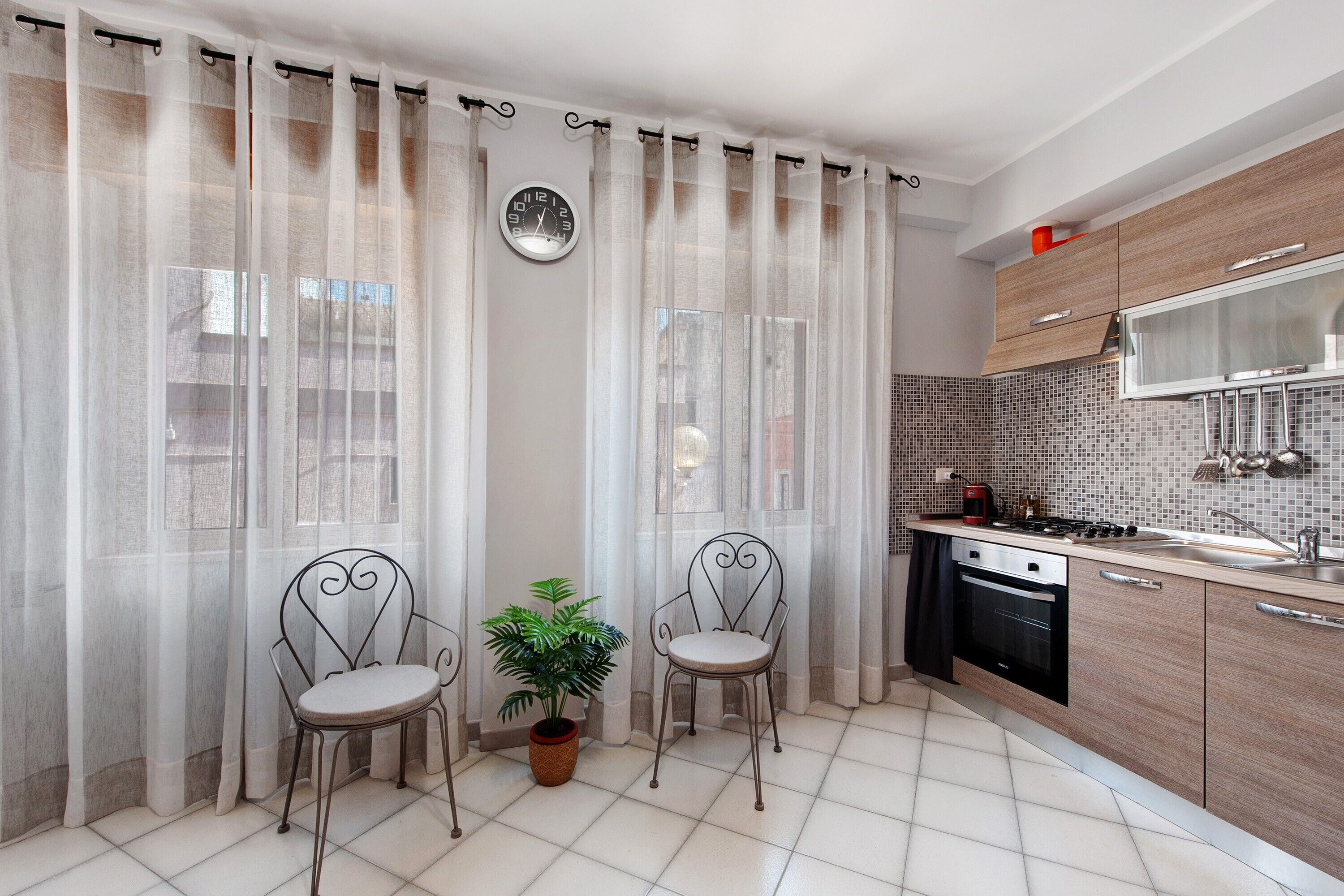 A modern kitchen with a gas stove, a dishwasher, and a tiled backsplash. There are two chairs with a potted plant between them.
