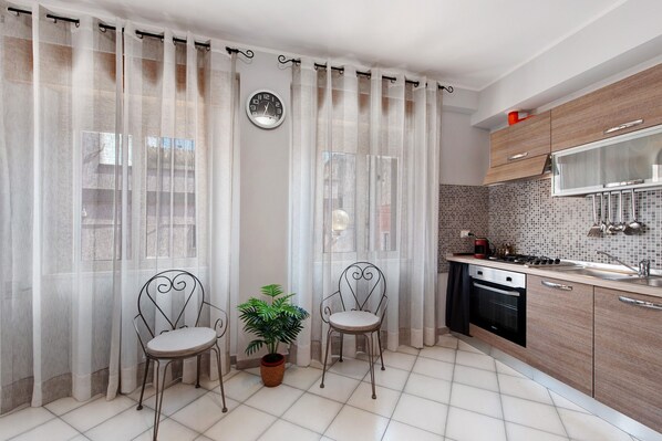 A modern kitchen with a gas stove, a dishwasher, and a tiled backsplash. There are two chairs with a potted plant between them.
