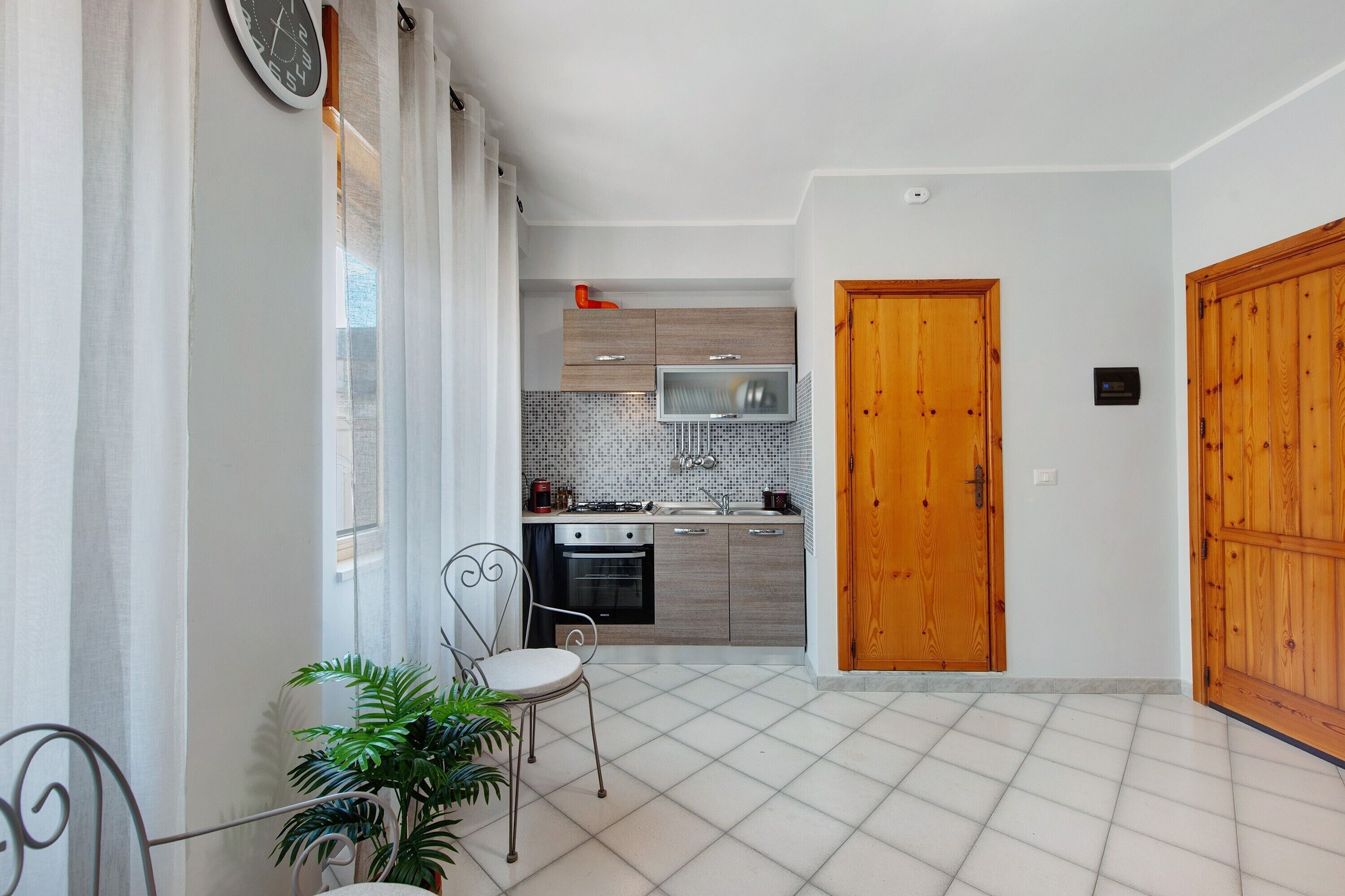 A modern kitchen with a microwave, oven, and sink. There is a wooden door and a potted plant.