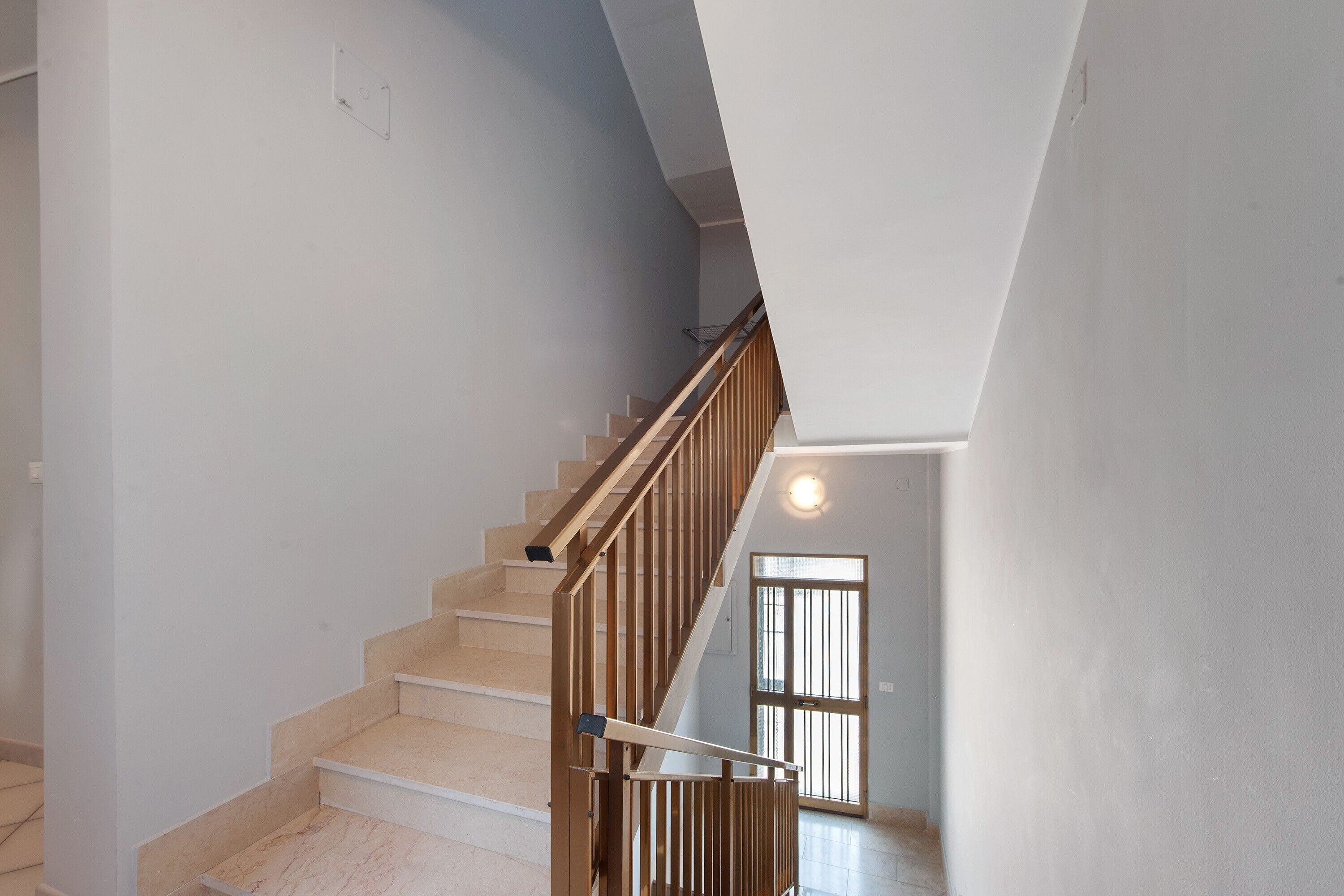 Eine Treppe mit hölzernen Geländern und beigefarbenen Stufen, die zu einer Zwischenebene führen.