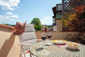 A round metal table with two wine glasses and a bowl of pastries, a white chair, and a straw hat on the chair. - Terrazzino San Frediano - Flo Apartments (Florence)
