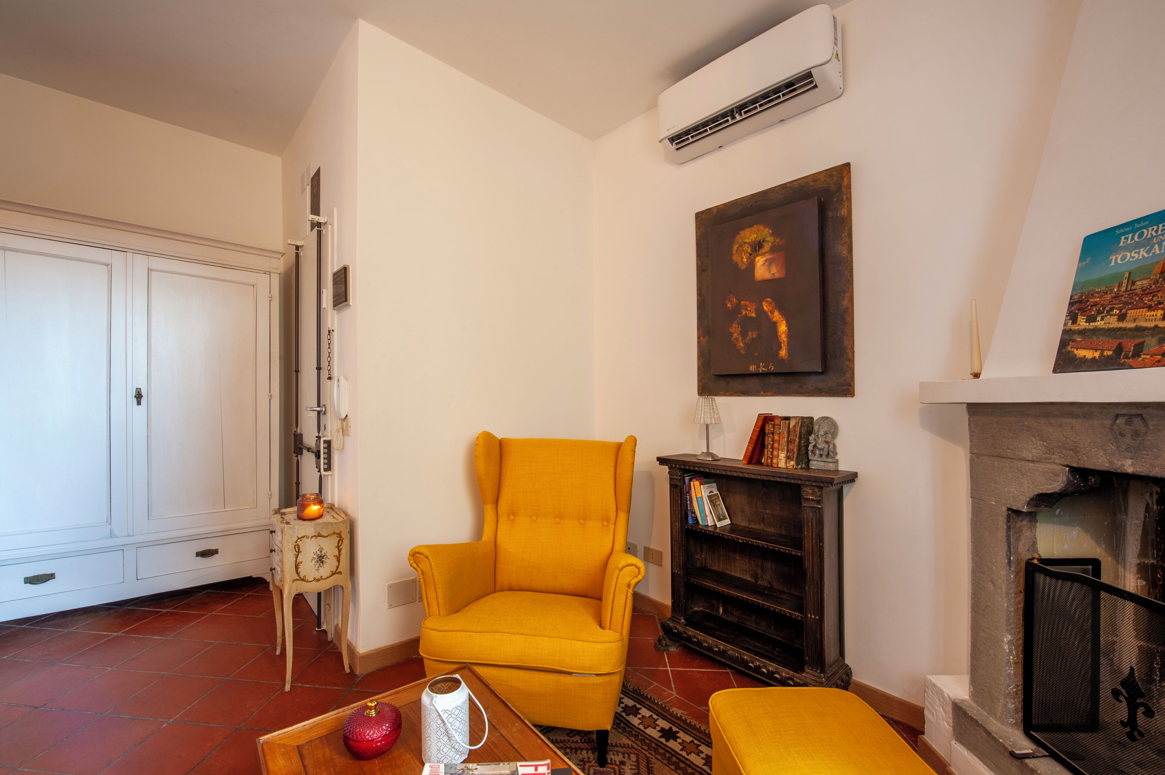 A living room with a yellow armchair, a fireplace, a bookshelf, and a white wardrobe.