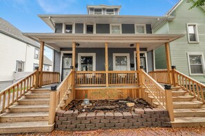 A two-story house with a front porch, wooden stairs, and a brick foundation. - Charming 2BR Retreat | Fully Equipped | Near German Village | 30+ nights (Columbus)